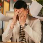 Stressed businessman overwhelmed by paperwork in office environment, demonstrating burnout.