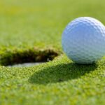 Close-up of a golf ball near the hole on a sunlit golf course green.