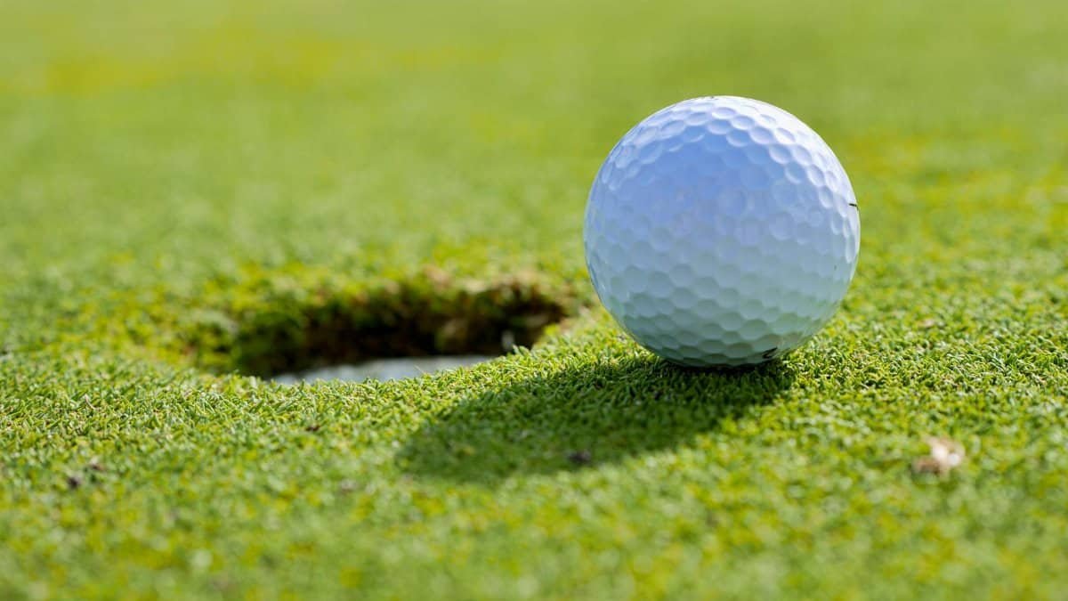 Close-up of a golf ball near the hole on a sunlit golf course green.