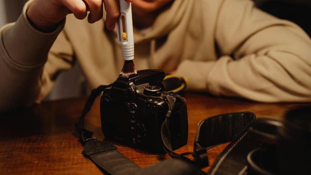 A person carefully cleaning a camera with a brush, emphasizing photography maintenance.