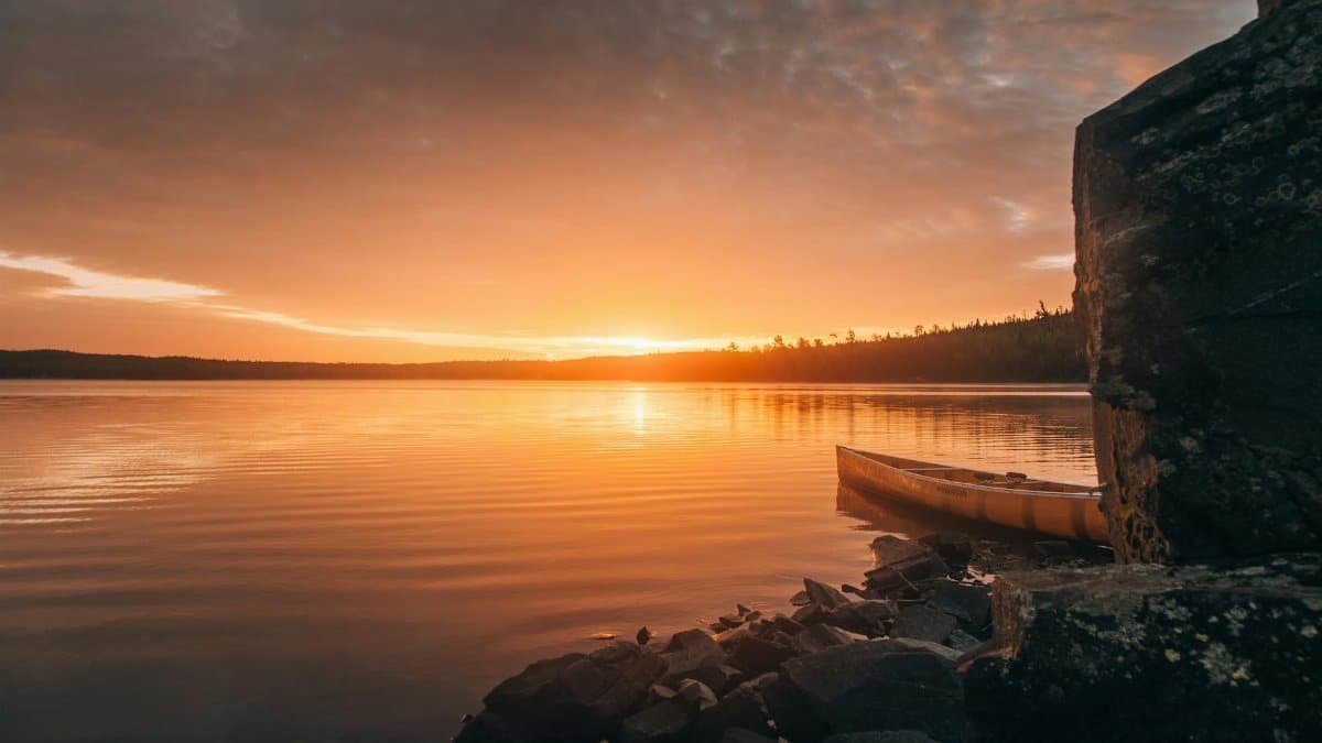 A tranquil sunset over a lake in Ely, Minnesota, featuring a canoe by the rocky shore.