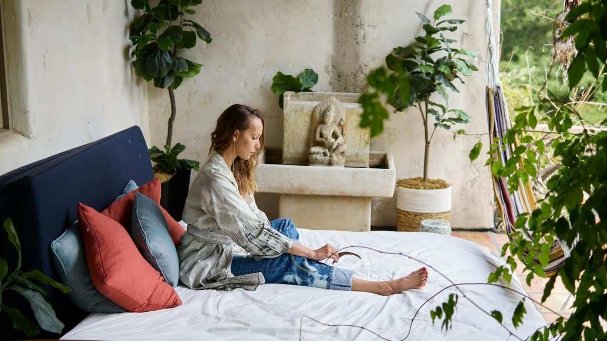 A woman relaxes in a cozy bedroom adorned with plants and elegant decor.