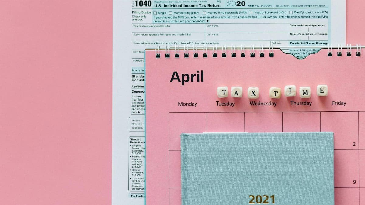 Flat lay image of tax forms, calendar, and 'tax time' reminder on a pink background.