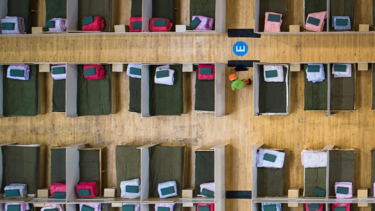 Top-down view of an emergency shelter with arranged beds in rows and worker present.