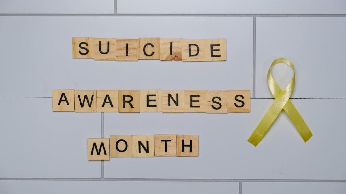 Wooden blocks spelling 'Suicide Awareness Month' with a yellow ribbon.
