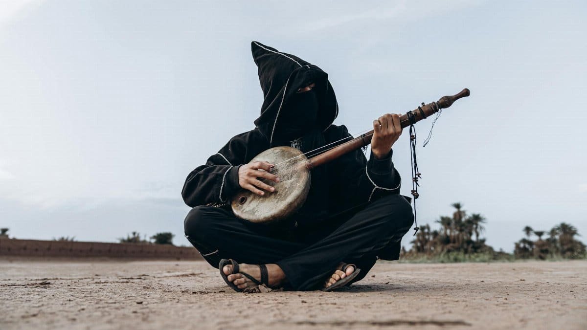 A masked musician plays an instrument in the Moroccan desert near Mhamid, reflecting cultural heritage.