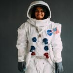 Portrait of a woman in a NASA astronaut costume, smiling against a neutral background.