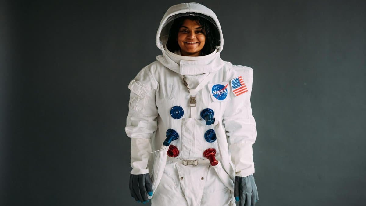 Portrait of a woman in a NASA astronaut costume, smiling against a neutral background.