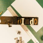 A top view of vintage printing tools including letter blocks, a ruler, and cutting tools on a green grid mat.