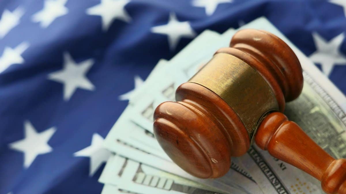 Close-up of a gavel on US dollar bills with American flag backdrop symbolizing justice and finance.