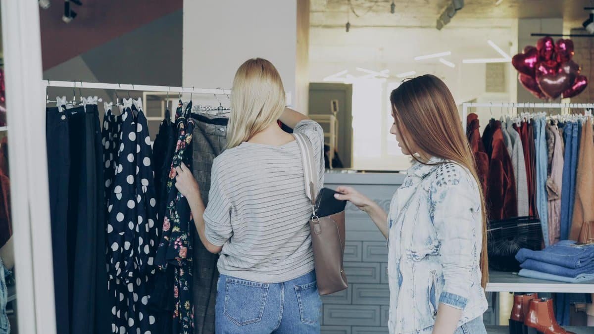 Two women browsing clothes in a boutique, exploring fashion choices indoors.