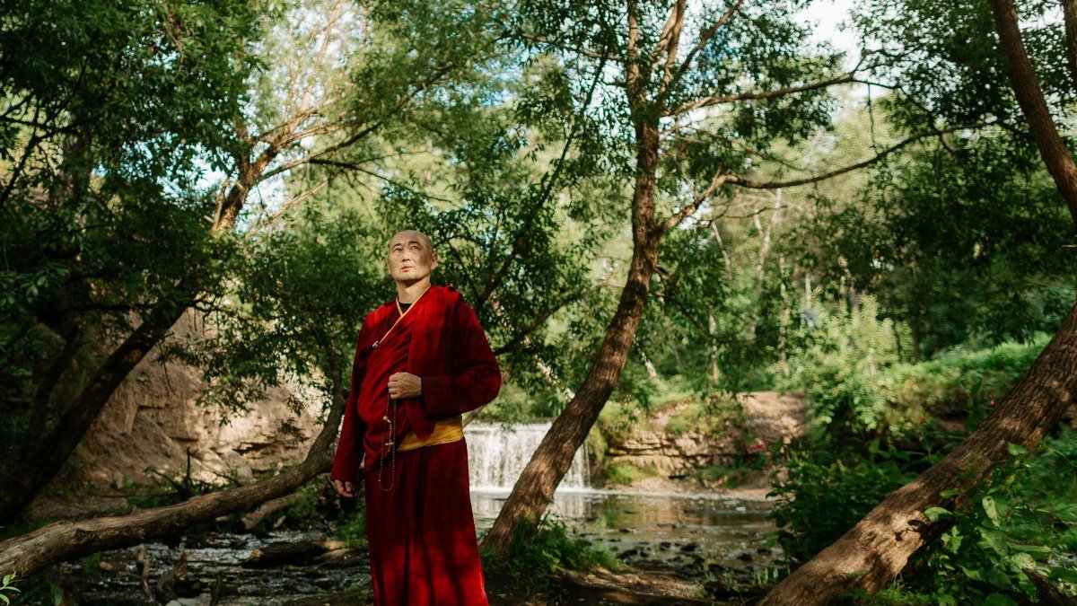A Buddhist monk stands peacefully in a lush forest near a serene waterfall, embracing nature.