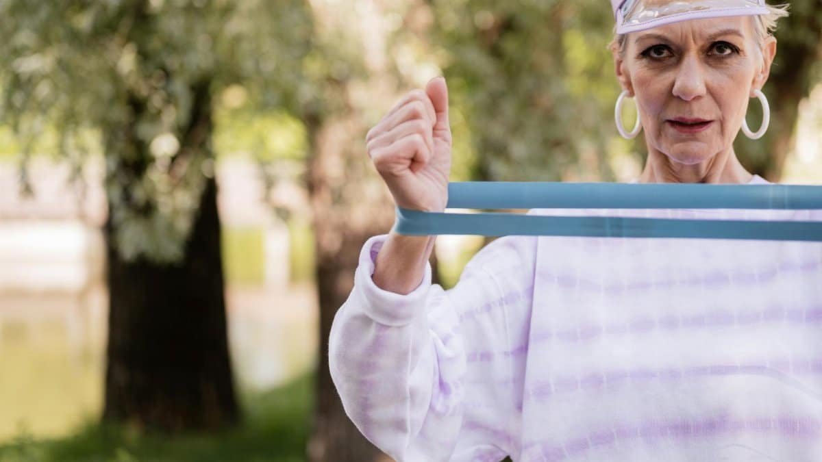 Caucasian senior woman working out with a resistance band in a park, showcasing healthy aging.