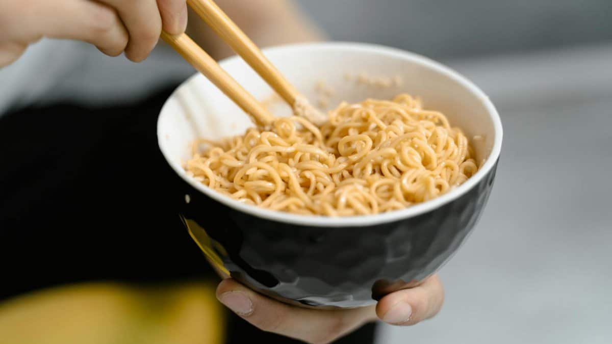 A person holding a bowl of noodles with chopsticks, captured in a close-up shot.