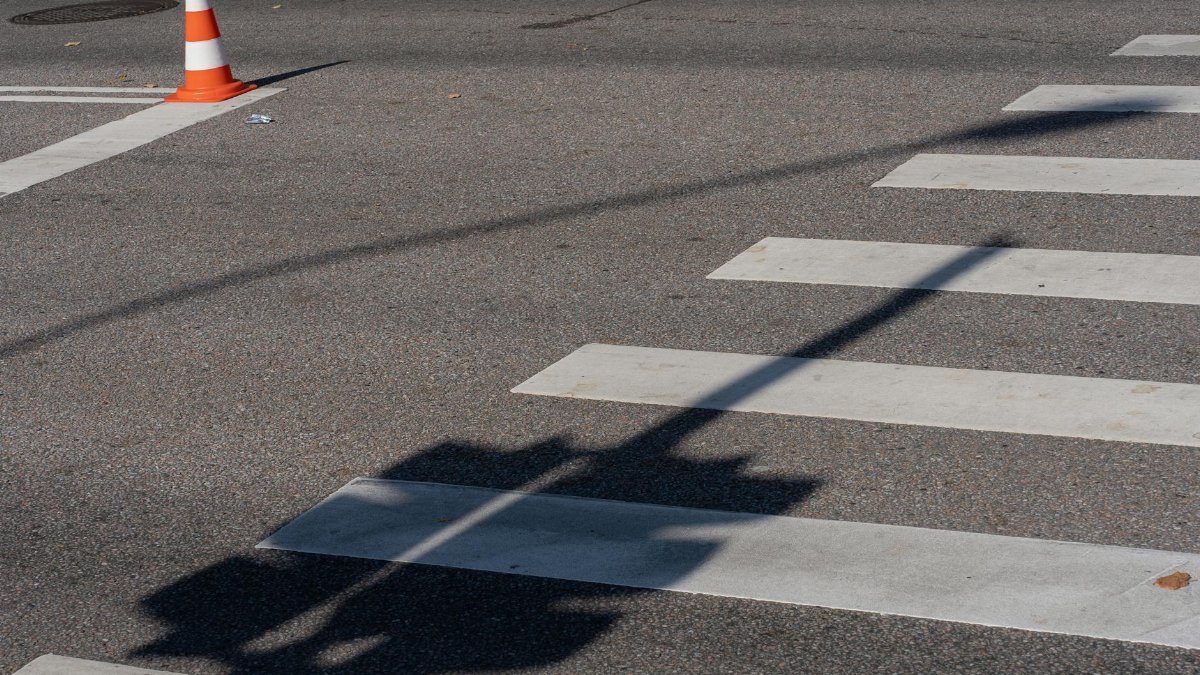 Street scene with a traffic cone, crosswalk, and shadows, capturing urban infrastructure.