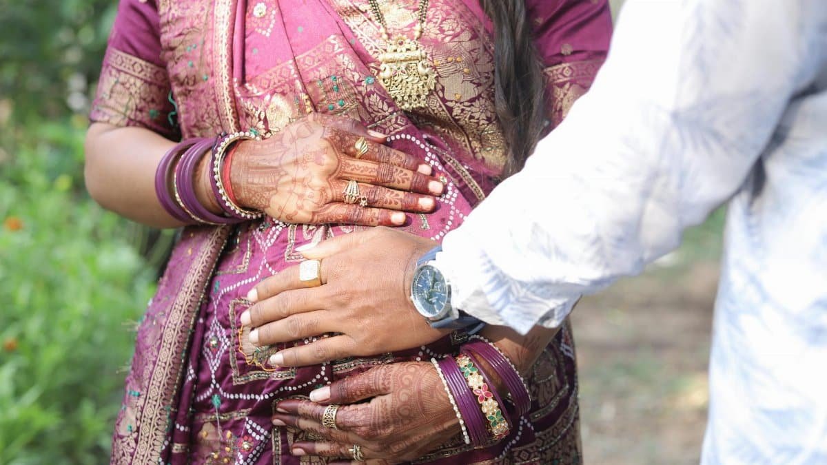 Pregnant woman in saree with partner outdoors, highlighting cultural beauty and family anticipation.