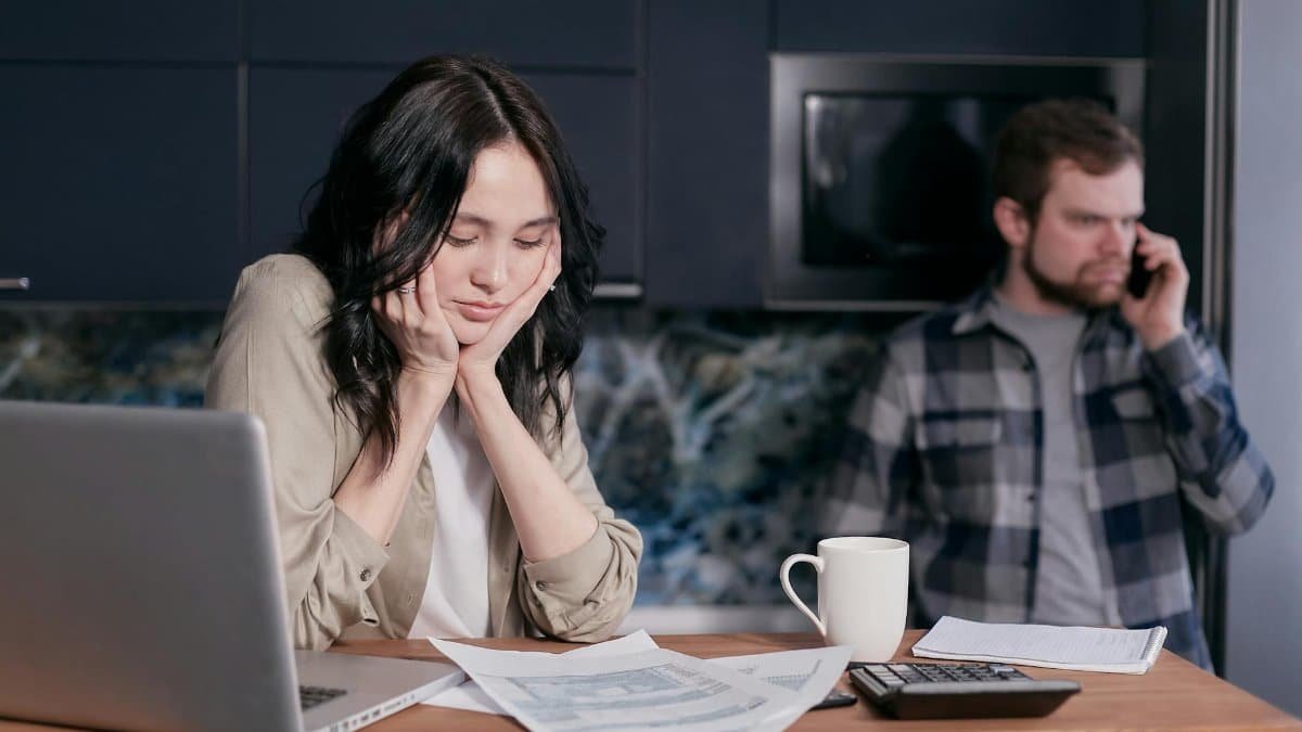 Couple dealing with financial stress at home, surrounded by bills and a laptop.