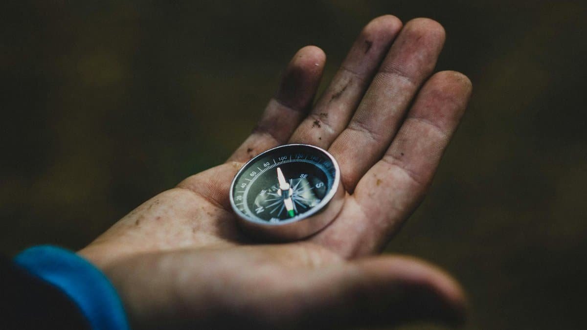 A close-up of a compass held in a dirty hand, symbolizing adventure and navigation.