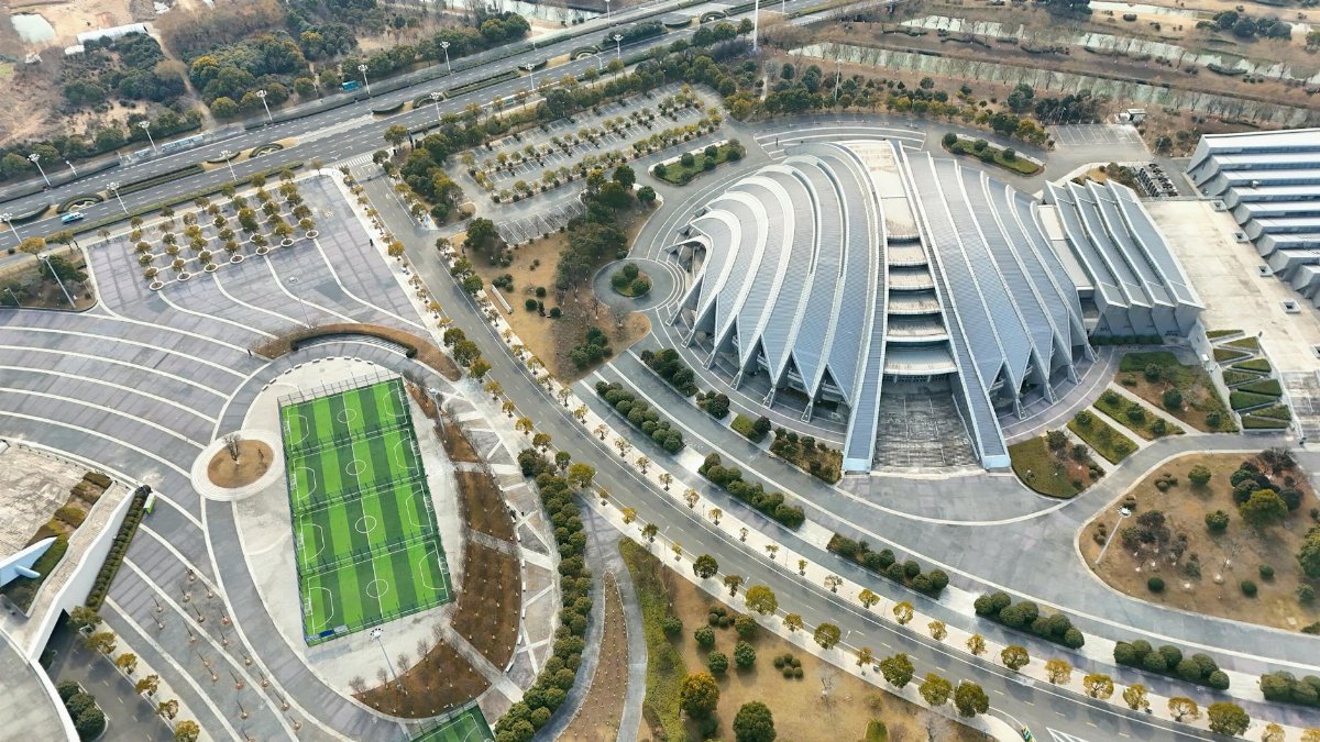 Aerial view of futuristic architectural complex with soccer field and parking lot.