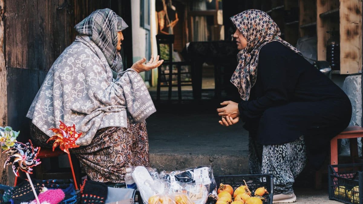 Two women converse at a market, showcasing traditional attire and local goods.
