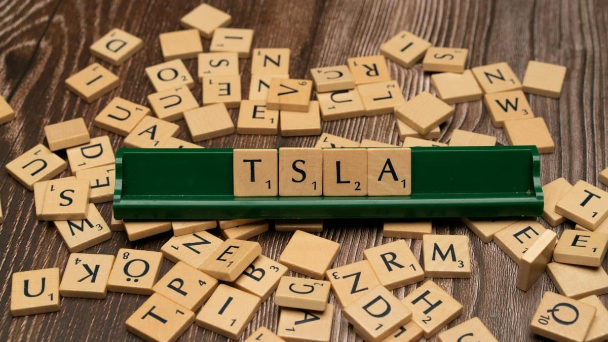 Wooden letter tiles spell TSLA, hinting at the stock market and investment themes.