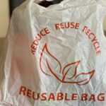 Reusable bag promoting reduce, reuse, recycle on a wooden table indoors.