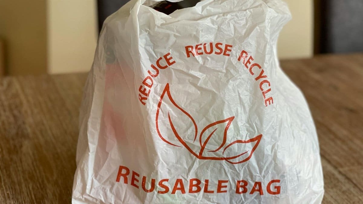 Reusable bag promoting reduce, reuse, recycle on a wooden table indoors.