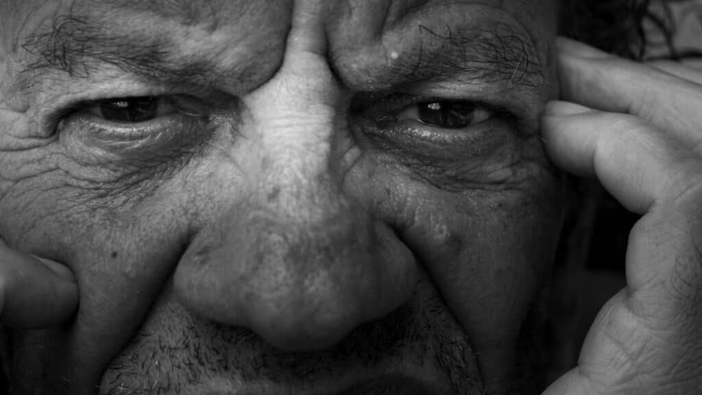 Black and white close-up of an elderly man's contemplative expression showing deep wrinkles and intense eyes.