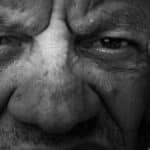 Black and white close-up of an elderly man's contemplative expression showing deep wrinkles and intense eyes.