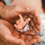 A senior adult's hands gently cradling a newborn's hand, symbolizing generational bonding and growth.