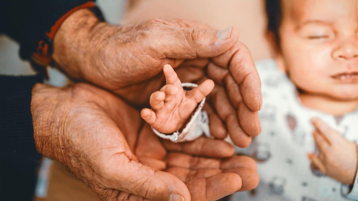 A senior adult's hands gently cradling a newborn's hand, symbolizing generational bonding and growth.