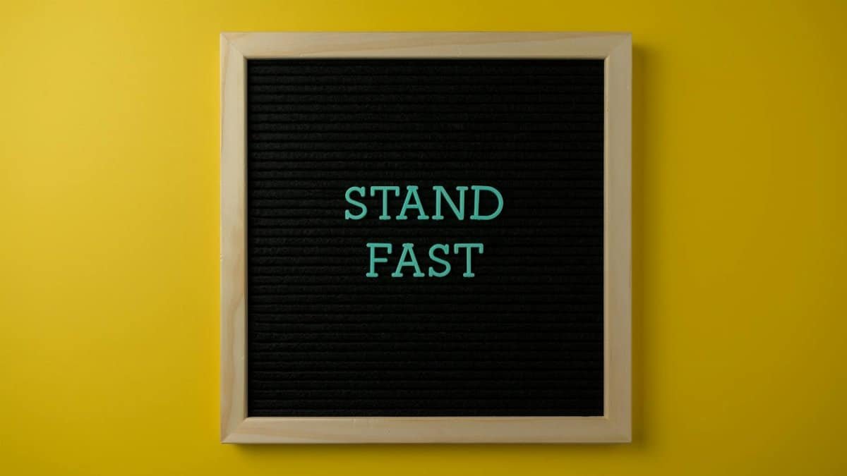Black letter board with 'Stand Fast' text against a vibrant yellow background.