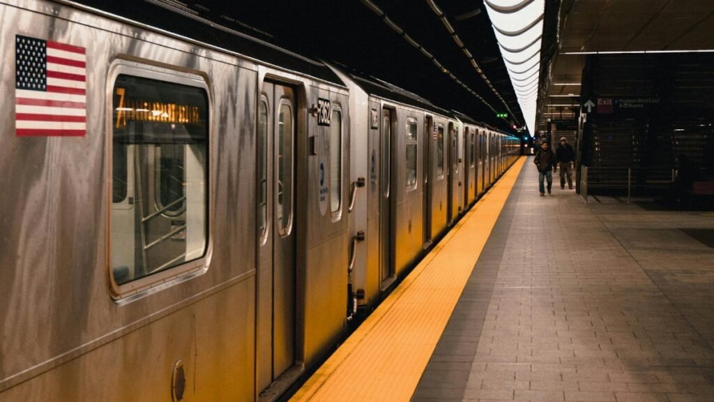 Image of a New York subway train at an underground station platform with an American flag.