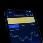 Close-up of a smartphone screen displaying a stock trading app with candlestick charts, showing real-time stock data.