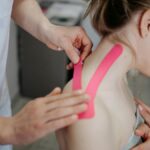 A physiotherapist applies kinesio tape to a woman's shoulder for pain relief and treatment.