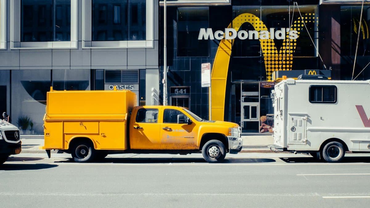 A yellow pickup truck parked in front of a McDonald's in New York City on a sunny day.