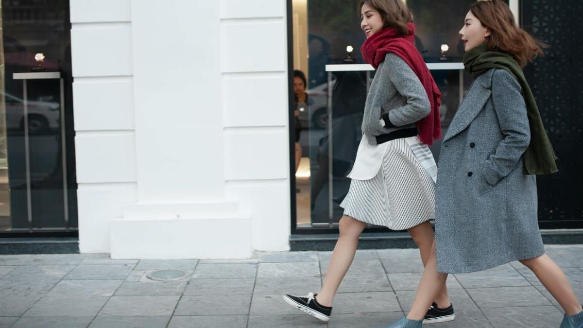 Two stylish women walking downtown in cozy coats and scarves on a chilly day.