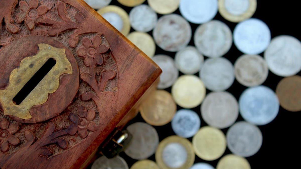 Beautifully carved wooden coin box surrounded by assorted coins, showcasing Indian craftsmanship.