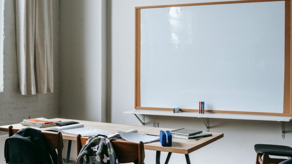 Classroom interior with whiteboard against student desk with notebooks and stationery in modern school