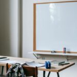 Classroom interior with whiteboard against student desk with notebooks and stationery in modern school