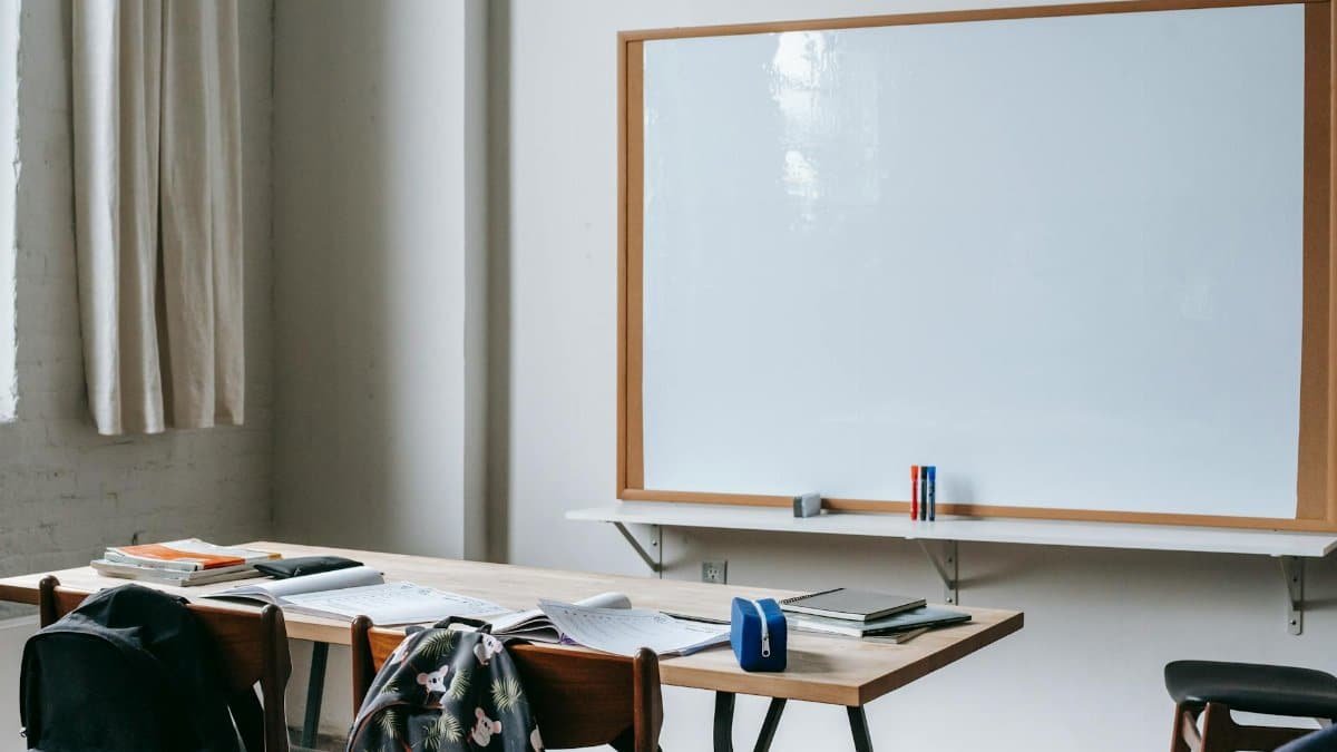 Classroom interior with whiteboard against student desk with notebooks and stationery in modern school