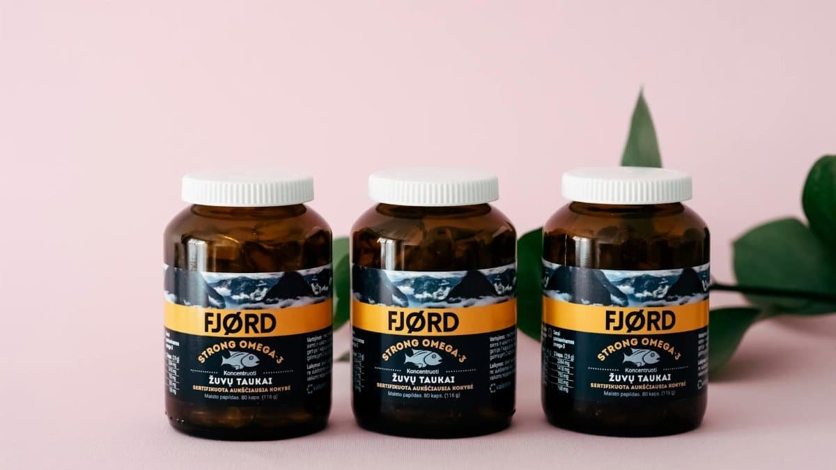 Three FJORD Omega-3 supplement bottles on a pink backdrop with greenery accents.