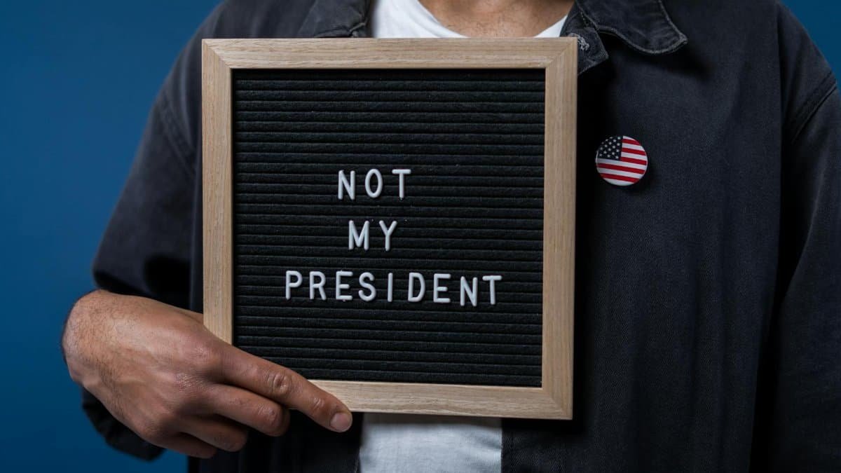 Person holding a letter board with 'Not My President' message and an American flag pin.