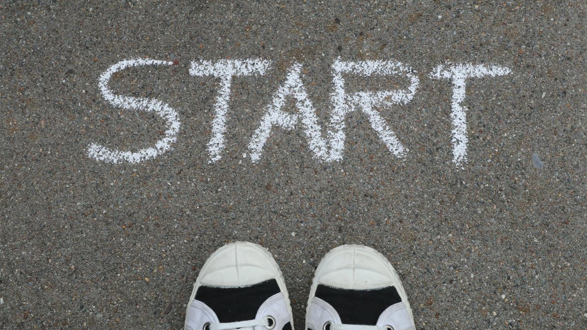Close-up of sneakers and a 'START' chalk drawing on pavement, symbolizing new beginnings.