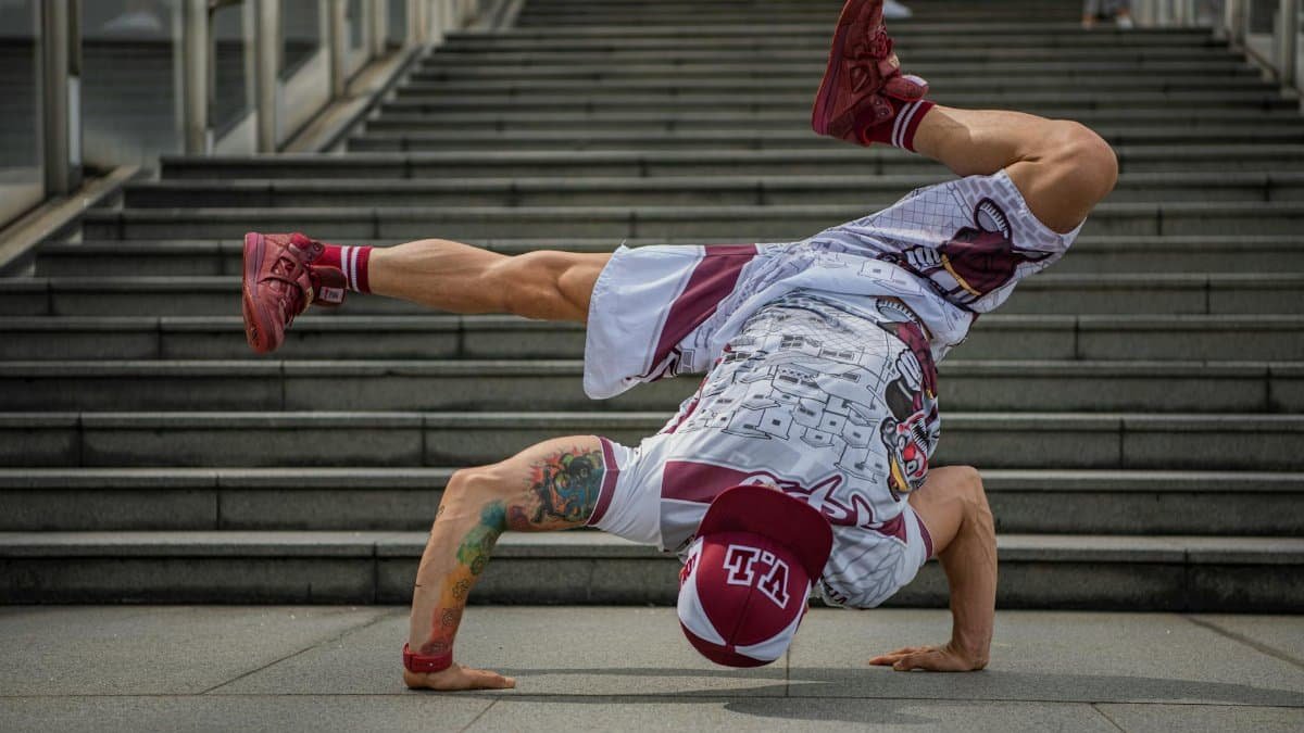 Dynamic breakdancer executing a freeze on city stairs in colorful attire.