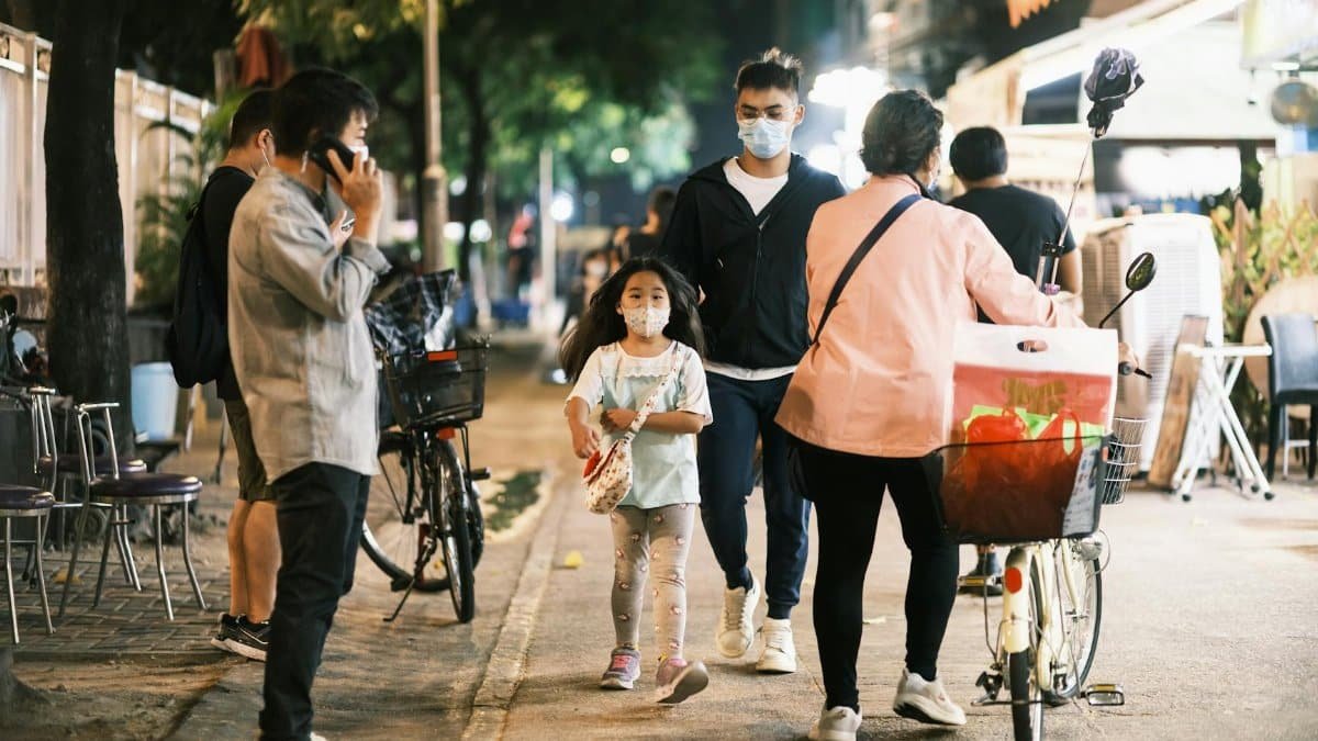 Urban street at night with people wearing face masks, depicting a scene of the new normal.