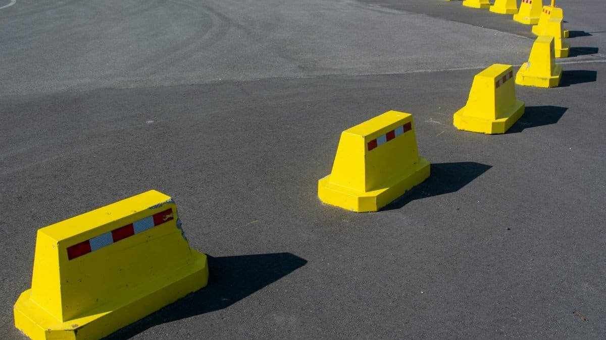Row of bright yellow traffic barriers on an empty asphalt road.