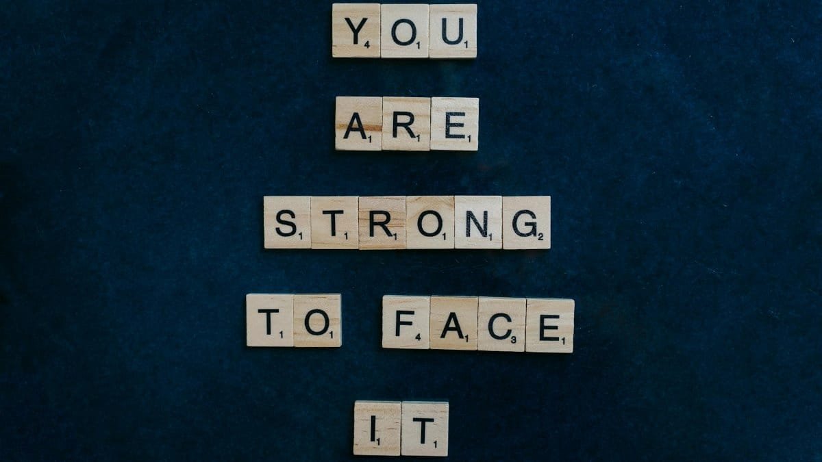 Scrabble tiles spelling 'You Are Strong To Face It' on a dark surface, conveying empowerment.