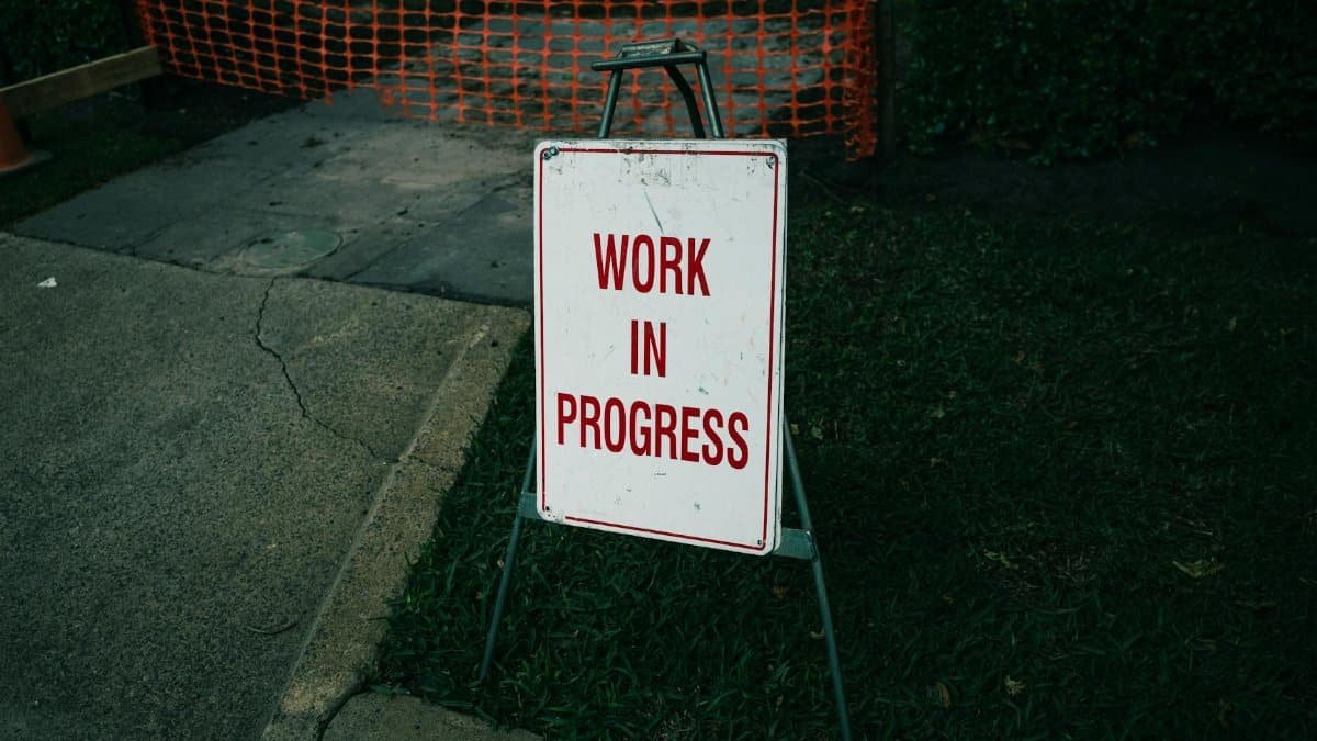 A 'Work in Progress' sign stands on a sidewalk next to safety barriers.