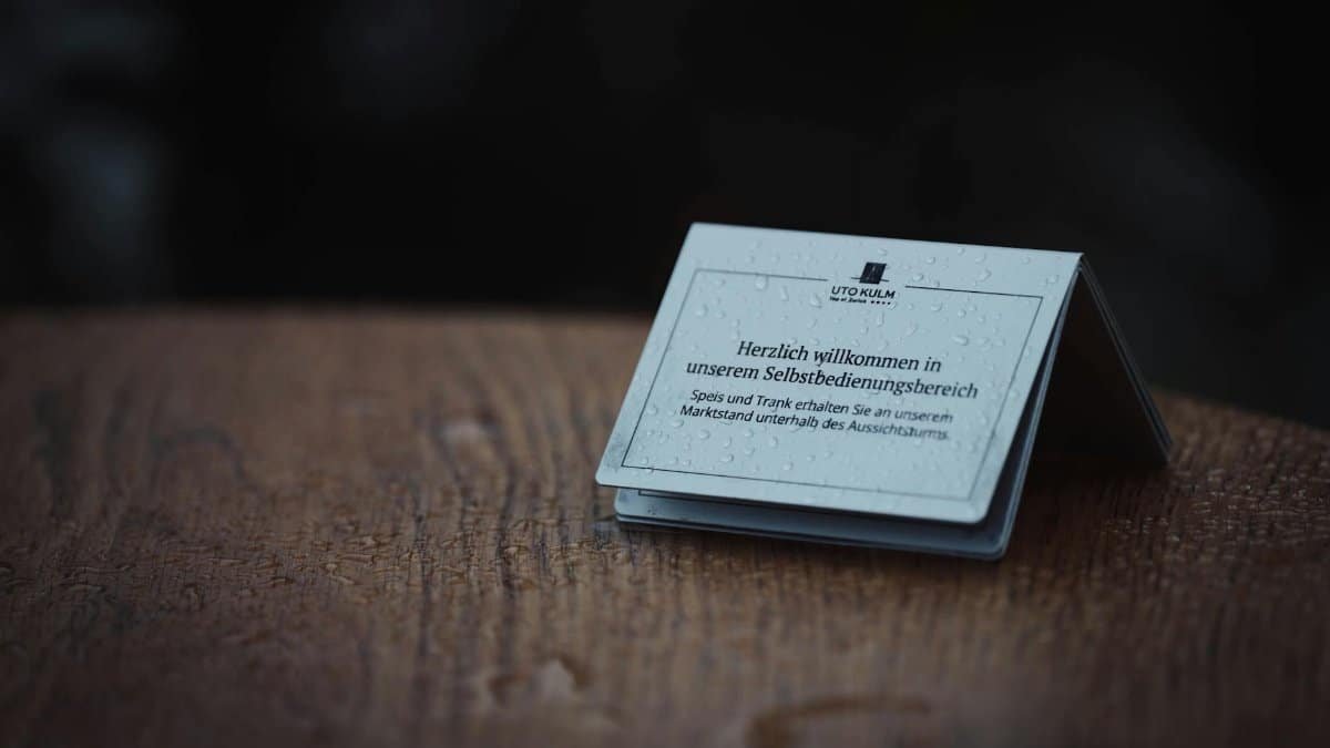 Raindrop-covered welcome sign at UTO Kulm on a wooden table outdoors.